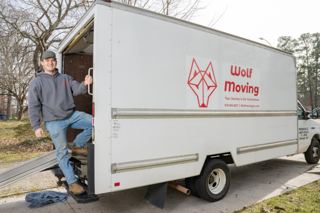 Wolf moving owner standing on the back of a moving truck smiling.