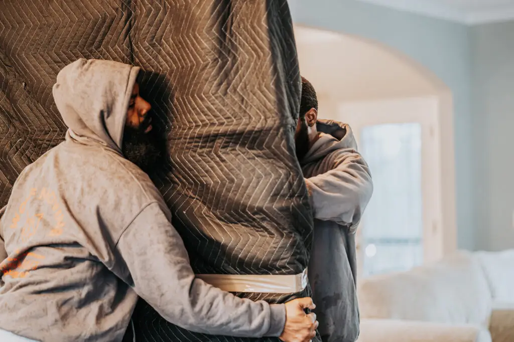 Two wolf moving employees carrying a table top wrapped in moving blankets