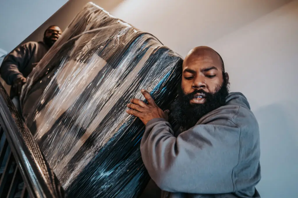 Wolf moving employees carrying wrapped furniture down stairs