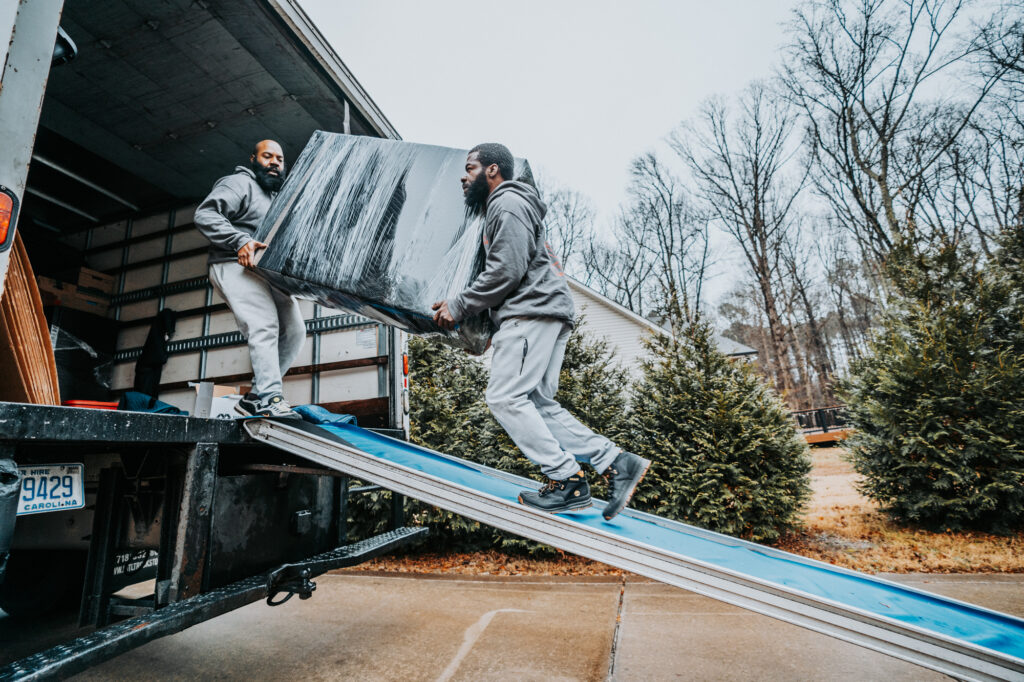 Two Wolf Moving employees loading wrapped furniture onto a truck.